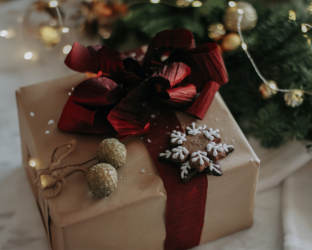 Božićni dar zamotan u papir, vezan mašnom i ukrašen kolačićem.