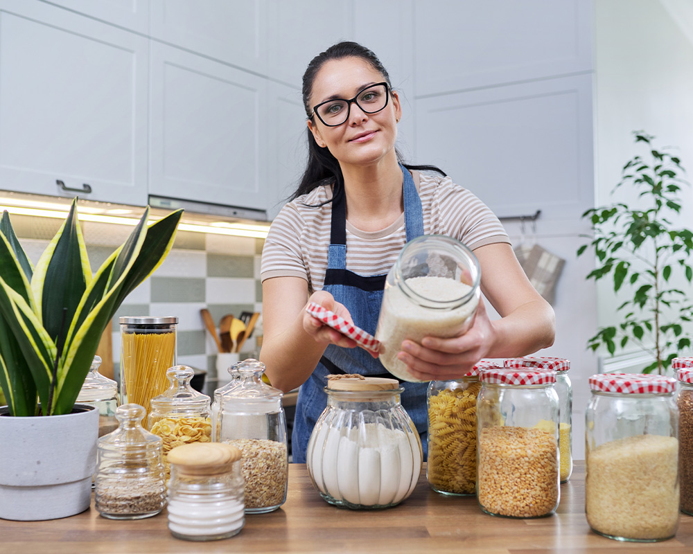 Žena u kuhinji pokazuje staklenke za pohranu suhe hrane