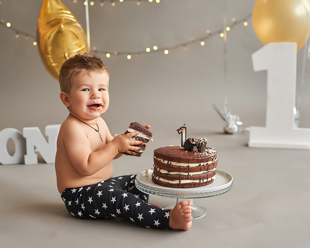 Jednogodišnji dječak drži komad čokoladne torte u rukama za rođendan