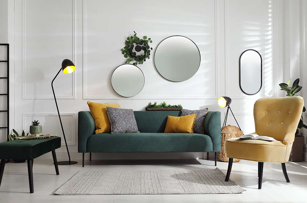 Moderan dnevni boravak u svijetlim bojama sa zelenom sofom, žutim jastučićima i okruglim ogledalima na zidu.