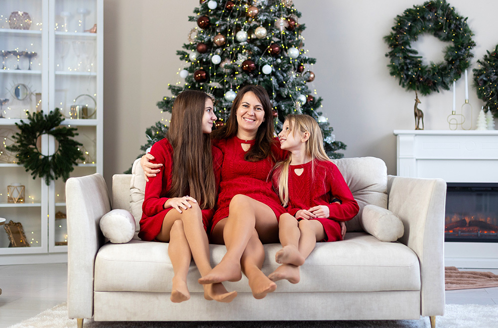 Mama i njezine kćeri u crvenim haljinama provode božićno vrijeme zajedno kraj bora
